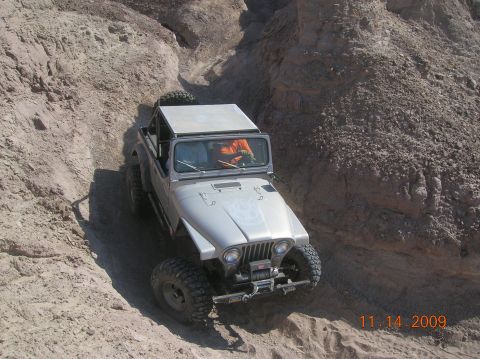 1985 Ford Bronco - A silver Jeep CJ-7 navigates a narrow dirt path between rocky inclines.