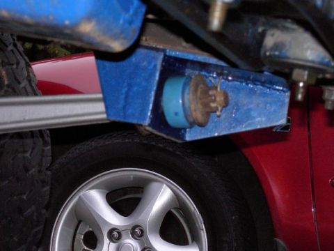 1980 Ford Bronco - Detail of a blue bracket and suspension component on a red vehicle, with a silver alloy wheel in the foreground.