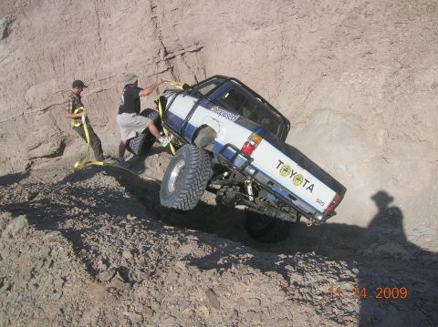 1985 Ford Bronco - Two people attempt to free a stuck Toyota pickup truck on a steep dirt incline.