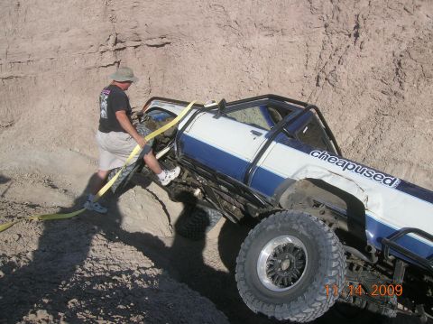 1985 Ford Bronco - A man uses a yellow strap to pull a stuck off-road truck out of a dirt embankment.