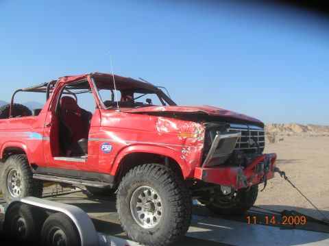 1985 Ford Bronco - This heavily modified 1985 Ford Bronco, seen on a trailer, shows significant damage to its front end and a reinforced roll cage.