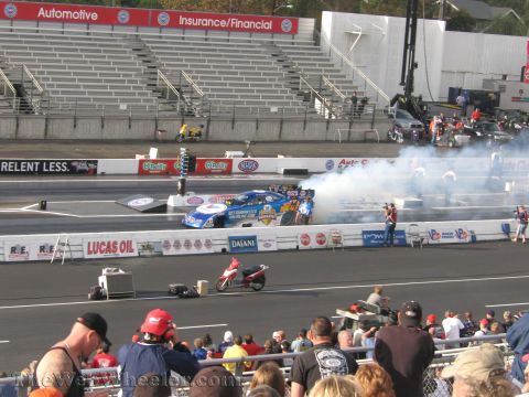 1968 Ford Mustang - A drag racing car generates smoke on the track during a qualifying event, with spectators watching from the stands.