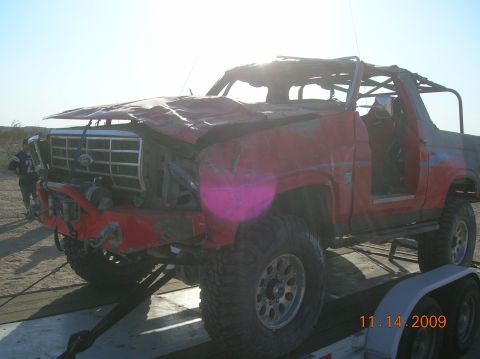 1985 Ford Bronco - This heavily damaged 1985 Ford Bronco is loaded onto a trailer, showing significant front-end collision impact.