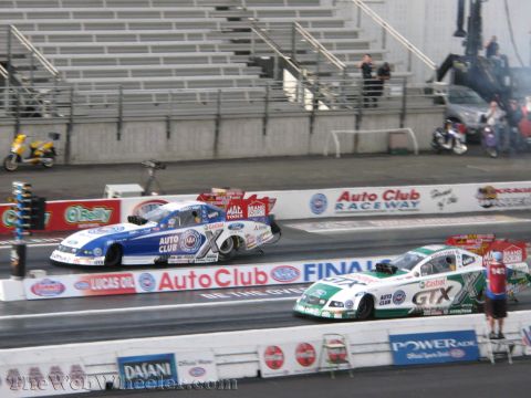 1968 Ford Mustang - Two dragsters compete side-by-side on a race track, with spectators in the stands and various sponsor logos visible.