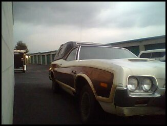 1972 Ford Ranchero - 1972 Ford Ranchero with wood paneling and a camper shell parked outside storage units.