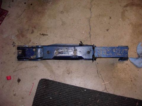 1980 Ford Bronco - A blue metal automotive part, likely a crossmember, lies on a concrete floor.