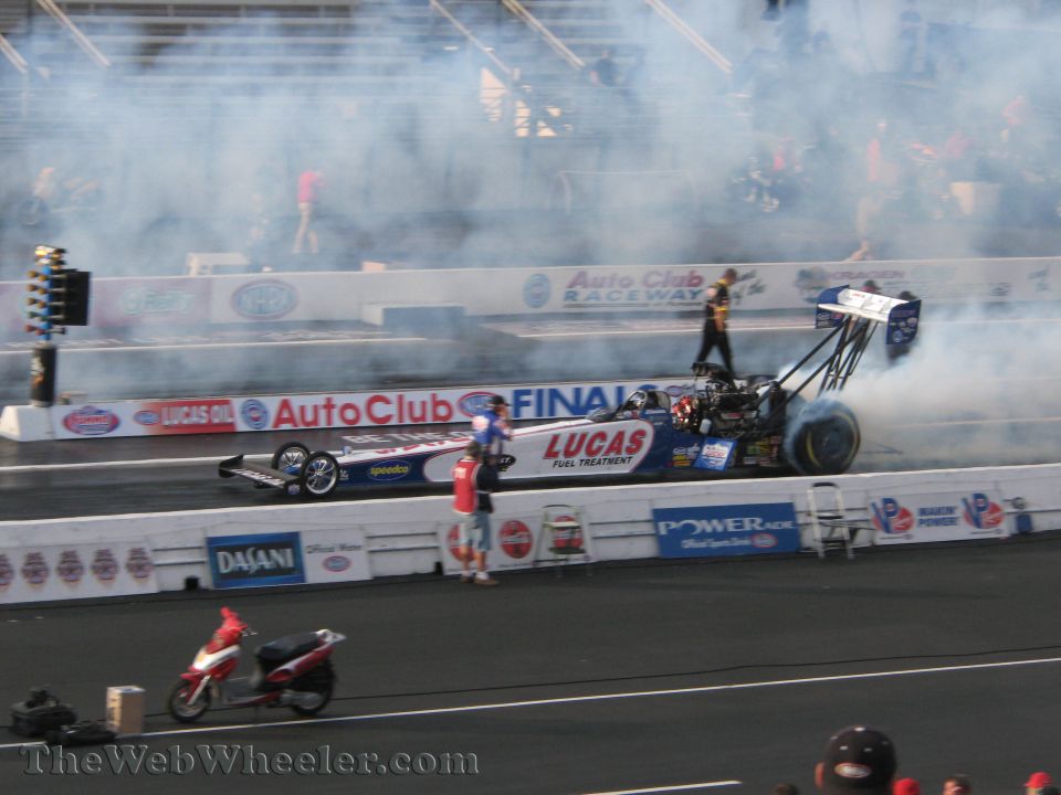 Blue and white dragster with Lucas Fuel Treatment livery, emitting smoke from rear tire