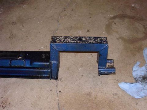 1980 Ford Bronco - A blue metal automotive part, possibly a transmission crossmember, lies on a concrete surface next to a crumpled paper towel.