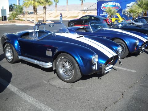 1986 Ford Bronco II - Multiple blue convertible sports cars are lined up in a parking lot under palm trees.