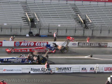 1968 Ford Mustang - Two dragsters compete on a track, with spectators in the stands and various sponsor logos visible on the barriers.