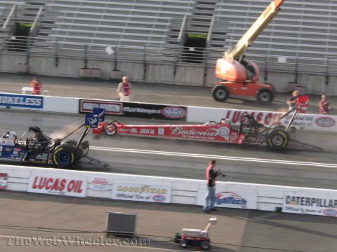 1968 Ford Mustang - Drag racing cars compete on a track, with spectators in the stands and a cherry picker visible in the background.