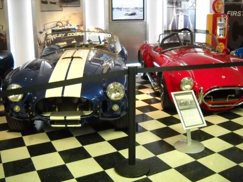 1986 Ford Bronco II - Two Shelby Cobra sports cars are displayed indoors with a vintage gas pump in the background.