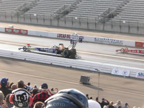 1968 Ford Mustang - Two drag racing cars compete on a track, with a crowd watching from the stands.