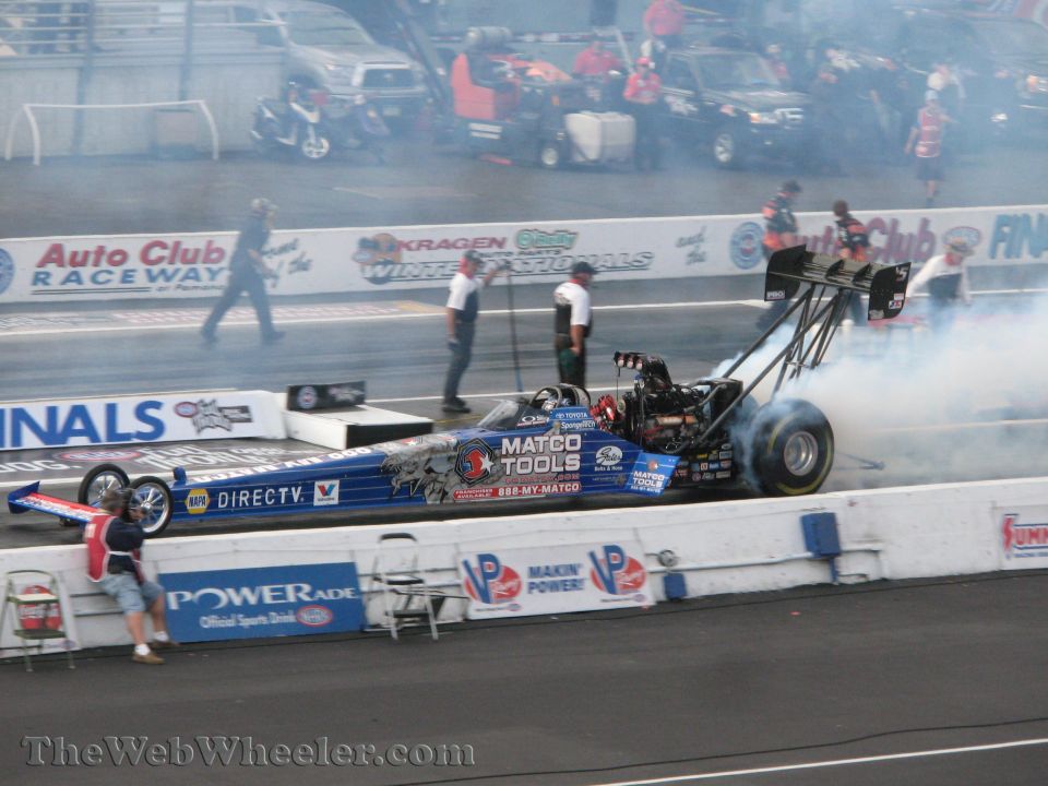Blue dragster with Matco Tools livery, emitting smoke from rear tires