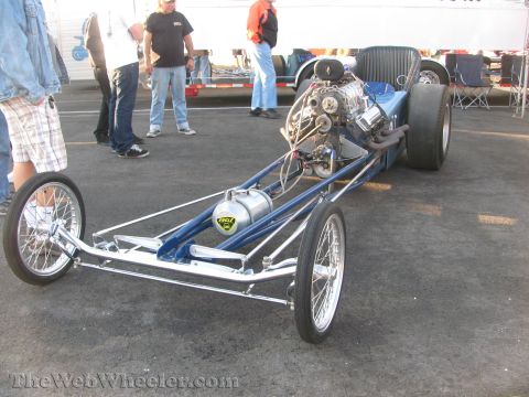 1968 Ford Mustang - A blue dragster with a prominent engine and large rear tires is parked on asphalt.