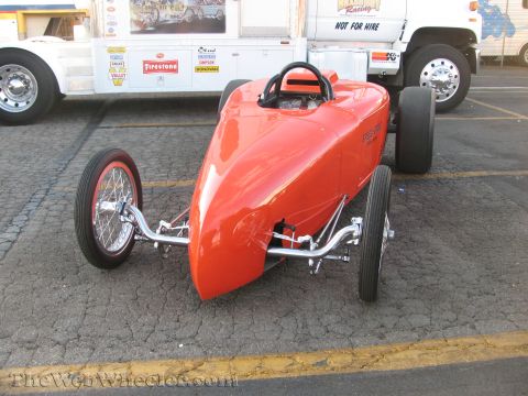 1968 Ford Mustang - An orange open-wheel race car is parked on asphalt, with a large white truck in the background.