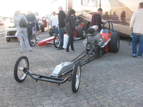 1968 Ford Mustang - A dragster with a prominent supercharged engine is parked on asphalt, with other vehicles and people in the background.