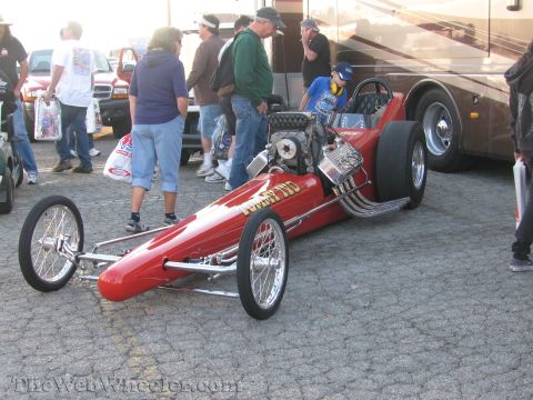 1968 Ford Mustang - A red dragster sits on asphalt with spectators around it.