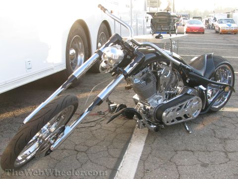 1968 Ford Mustang - A custom chopper motorcycle with a chrome skull headlight is parked on asphalt, with other vehicles and a trailer in the background.