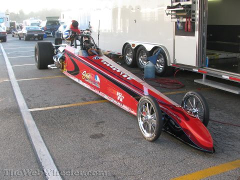1968 Ford Mustang - A dragster sits ready for action at a race track, with other vehicles and a trailer in the background.