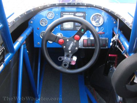 1968 Ford Mustang - The interior of a race car shows a blue roll cage, a black steering wheel, and a dashboard with multiple gauges and switches.