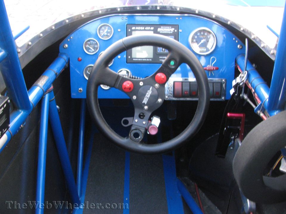 Racing car interior with blue roll cage, black steering wheel, and dashboard with gauges