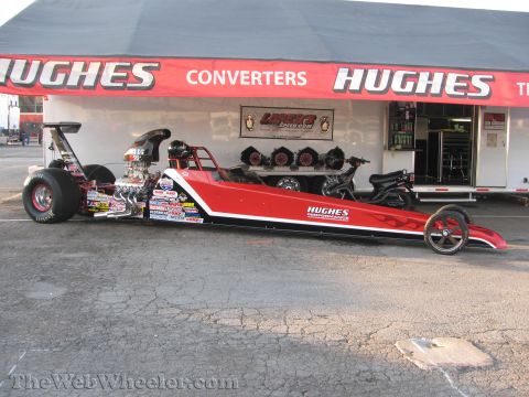 1968 Ford Mustang - A red dragster adorned with numerous sponsor decals and flame graphics sits parked in front of a Hughes Converters trailer.