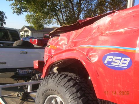 1985 Ford Bronco - A red SUV with extensive damage to its front end and hood is seen from the side, with an FSB logo on its door.