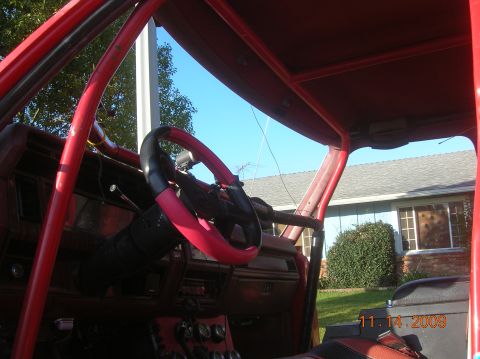 1985 Ford Bronco - The interior of a modified vehicle with a prominent red roll cage and a custom steering wheel is shown.