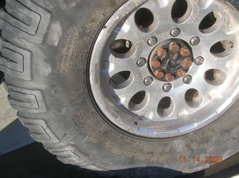 1985 Ford Bronco - A close-up view of a vehicle's tire and wheel assembly, showing tread detail and lug nuts.