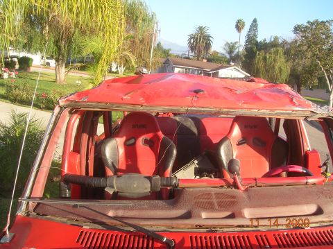 1985 Ford Bronco - Interior of a red vehicle shows racing seats and a heavily damaged roof structure.