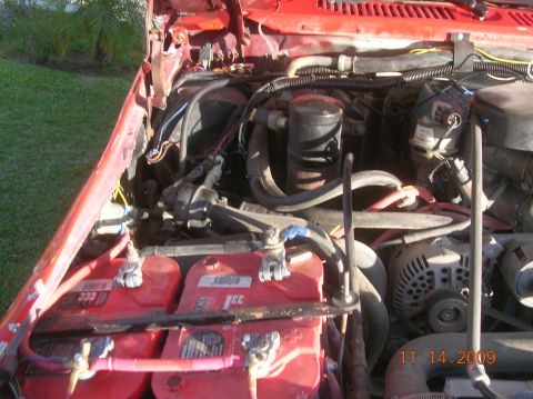 1985 Ford Bronco - The engine bay of a vehicle shows dual red batteries and various engine components under the hood.