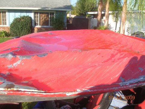 1985 Ford Bronco - The red car hood shows significant damage and peeling paint, with a residential house visible behind it.