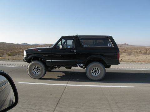 1986 Ford Bronco - Side view of a black Ford Bronco on a highway under a clear blue sky.