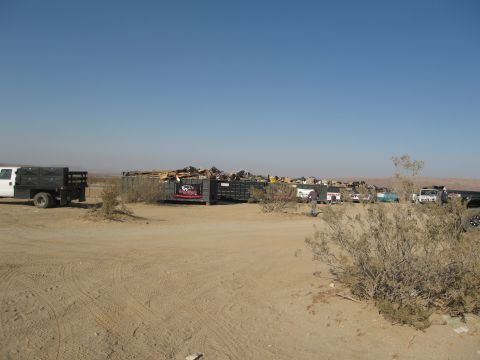 1986 Ford Bronco - A collection of vehicles and dumpsters are visible in a desert landscape during a cleanup event.