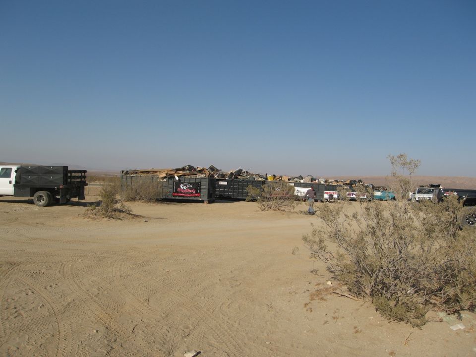 Desert scene with dumpsters and multiple vehicles under a clear blue sky