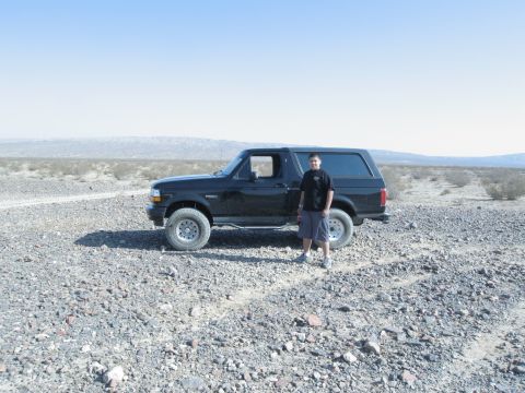1986 Ford Bronco - A man poses with his black Ford Bronco in a desolate, rocky desert environment under a clear blue sky.