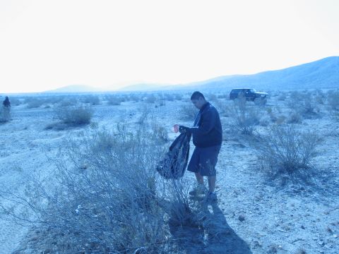 1986 Ford Bronco - A man collects trash in a desert landscape, with a vehicle visible in the distance.