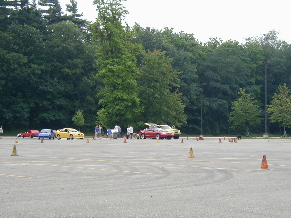 Autocross paddock in a parking lot with cones, red Mustang and yellow Neon