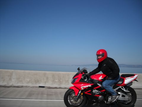 1991 Ford Bronco - A rider on a red motorcycle cruises along a highway with a body of water in the background.