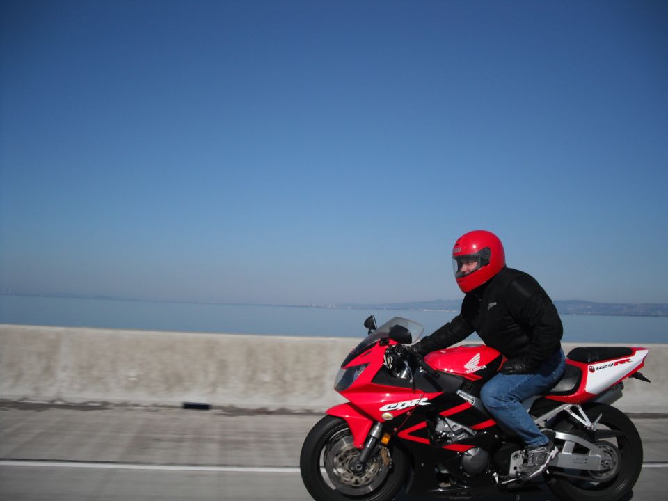 Red motorcycle with black accents and a rider wearing a red helmet and blue jeans, seen from the side