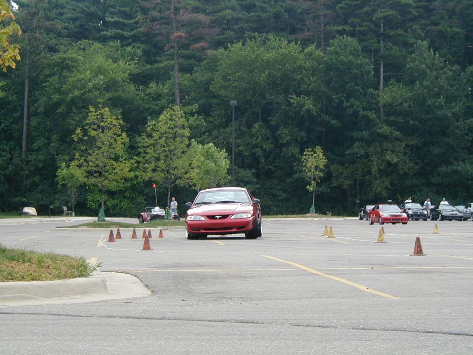 Red SN95 Mustang running an autocross cone course in a parking lot