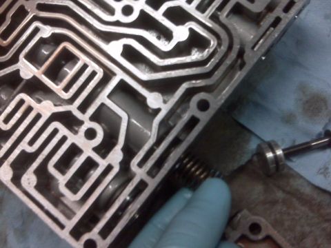 1994 Ford F-150 - A close-up view of a complex metal valve body, with a hand in a blue glove holding a spring and pin.