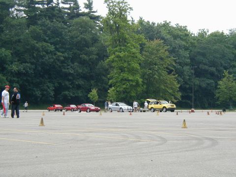 1994 Ford Mustang - Cars are lined up on a paved lot, with trees in the background and cones marking a course.
