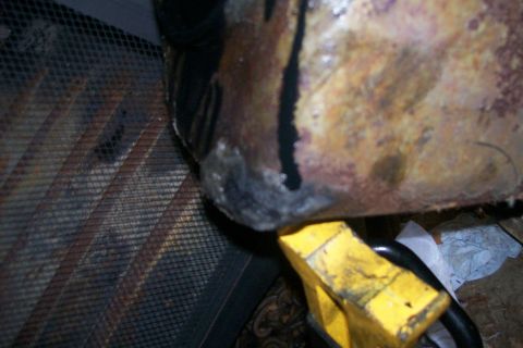 1992 Ford C-350 (Centurion Conversions) - A close-up view of a discolored and possibly damaged engine component supported by a yellow jack stand.