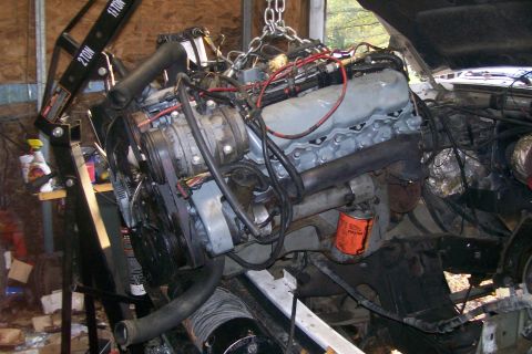 1992 Ford C-350 (Centurion Conversions) - An engine is being worked on, suspended by a hoist in a garage setting.