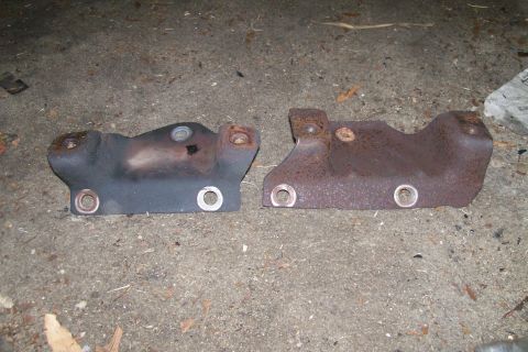 1992 Ford C-350 (Centurion Conversions) - Two exhaust manifold parts, one darker and less rusted than the other, lie on the ground.