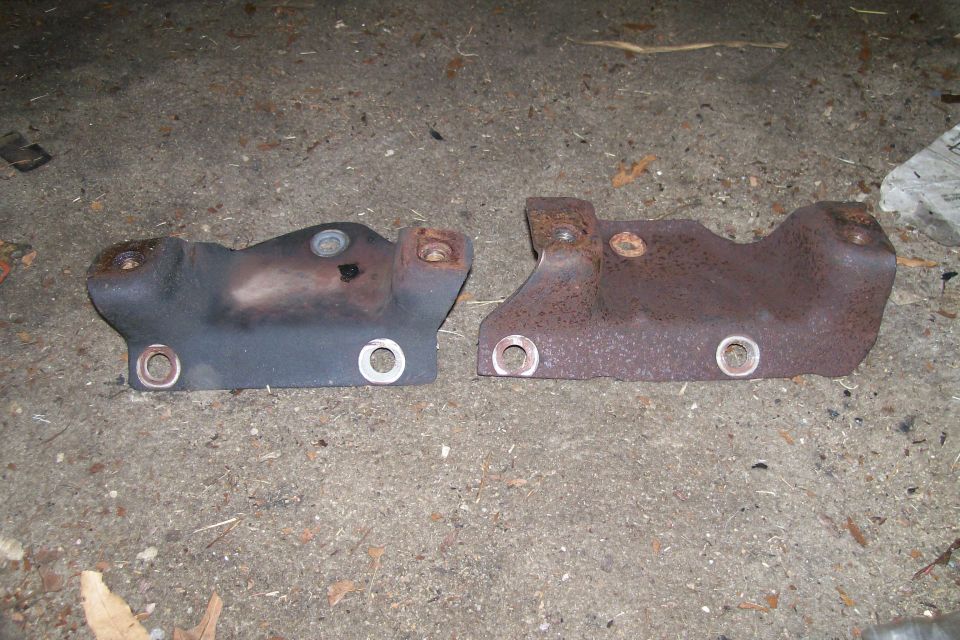 Two rusted metal exhaust manifold parts on a concrete surface