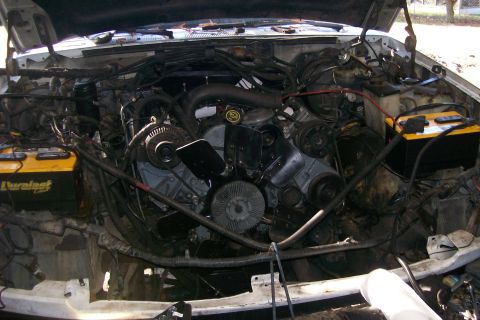 1992 Ford C-350 (Centurion Conversions) - The engine bay of a vehicle is shown with the hood open, revealing the engine components and two batteries.