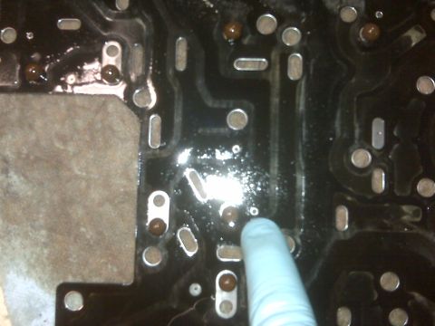 1994 Ford F-150 - A gloved finger points to a component on a dirty automatic transmission valve body, showing internal circuitry and external metal parts.